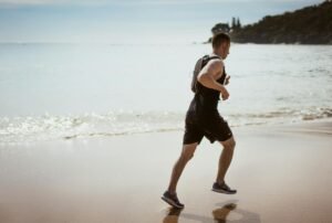 man wearing black tank top and running on seashore